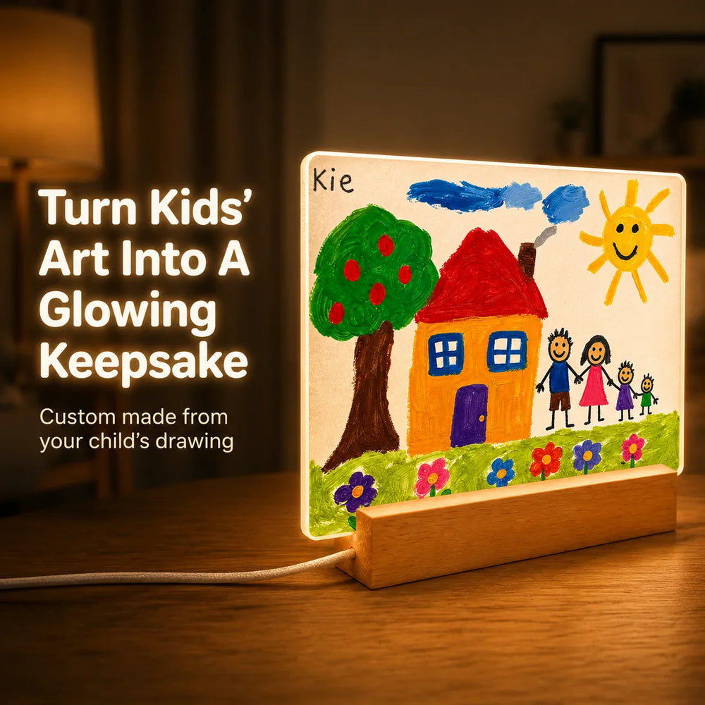 Kids drawing night light glowing on a bedside table, warm LED wooden base lighting up a child's painted house and family scene printed on clear acrylic.