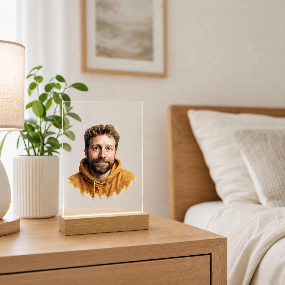 Acrylic photo portrait plaque with a watercolor portrait on a light wood nightstand beside a lamp and plant in a bright bedroom
