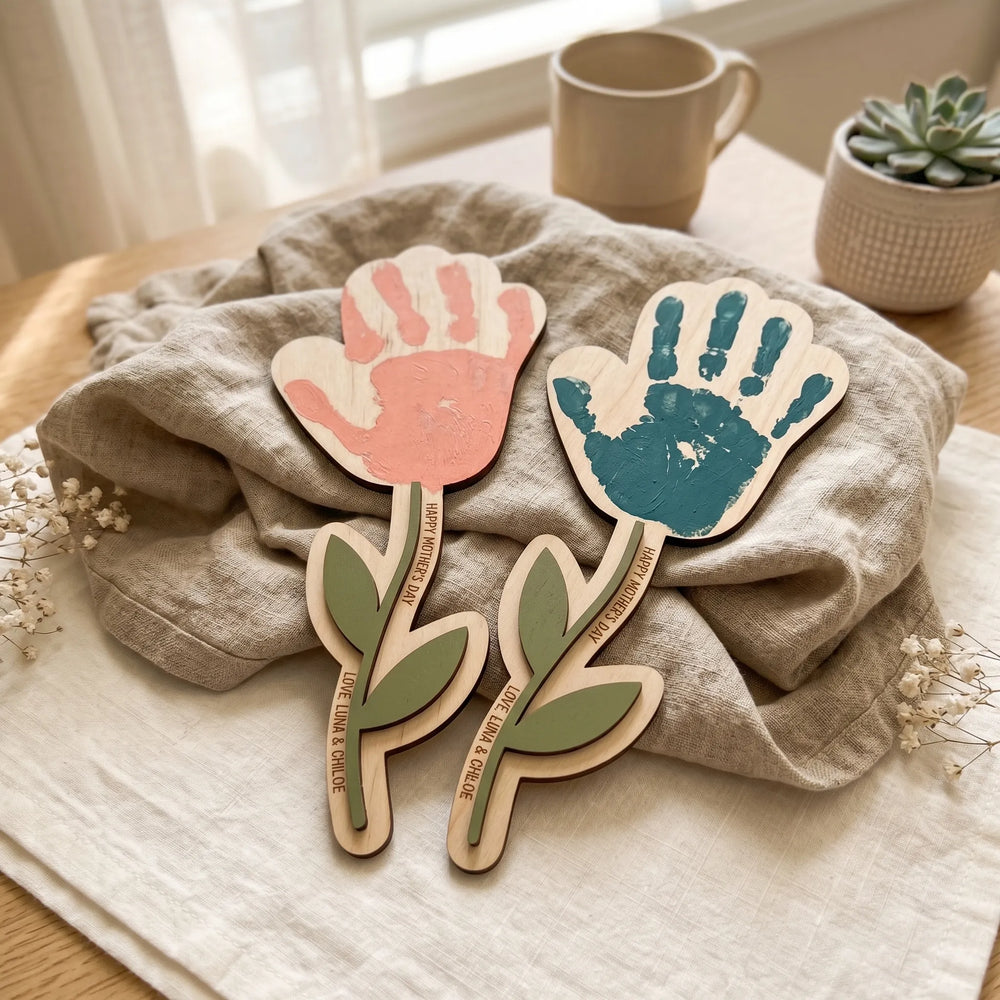 Two personalized Mother's Day handprint flower signs with pink and teal handprints and custom names engraved on maple wood